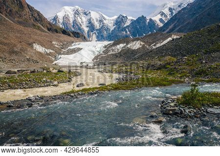 Sunny Alpine Landscape With Confluence Of Two Various Mountain Rivers On Background Of Snowy Mountai