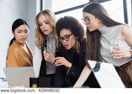 Afircan American Woman Pointing With Pen At Laptop Near Multicultural Managers
