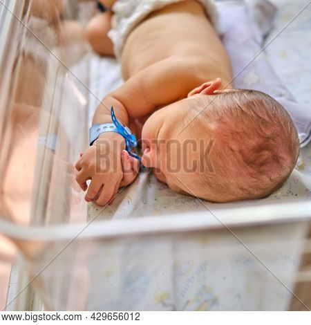 A Newborn Baby With A Maternity Hospital Bracelet On His Arm Is Sleeping In A Crib. A Newly Born Chi