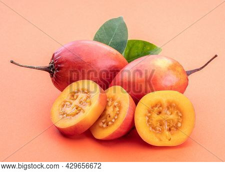 Ripe tamarillo fruits with slices and tamarillo leaves isolated on a orange background.