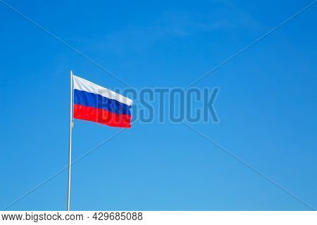 Russian Flag On A Pole Against Blue Sky. Copy Space