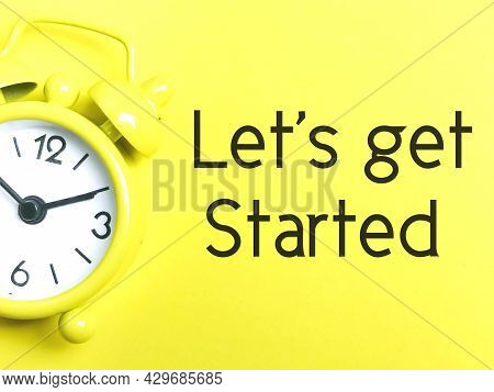 Phrase Lets Get Started Written On Yellow Background With Yellow Analog Alarm Clock.