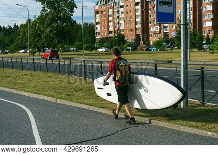 A Sporty Man Walks Through The City And Carries A Sup Board In His Hands.