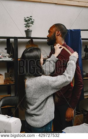 Corean Female Tailor Measuring Black Man In Workshop