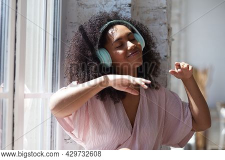 Happy Hilarious Black Multiracial Lady Wearing Headphones Near The Window