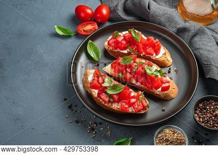 Three Bruschetta With Tomatoes, Basil And Cheese On A Black Plate. A Traditional Italian Snack. Side