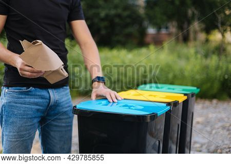 Close-up Of Man Throwing Peace Of Cardboard In Recycling Bins. Humen Hand Holding Paper Near The Pla