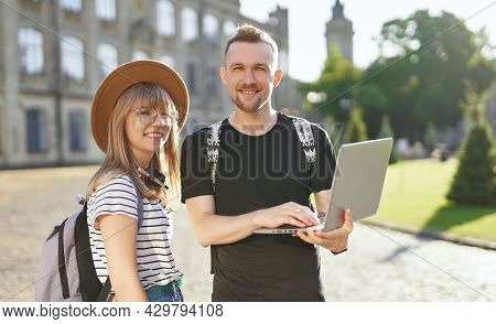 Studying Together. Two Cute Students, Male And Female, With Backpacks Using Laptop At The University
