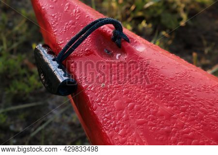 Drops Of Water And A Spider On The Bow Of A Red Plastic Kayak. Black Handle For Carrying The Boat.