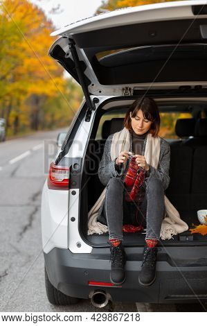 Pretty Caucasian Brunette Female In Grey Coat Sitting In Suv Trunk. Female Knittes Red Striped Socks