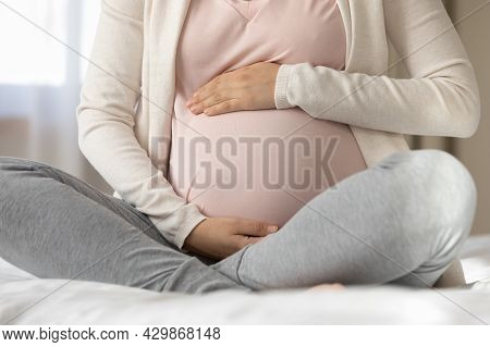 Late Pregnant Woman Sitting In Beddings, Touching, Caressing Baby Bump