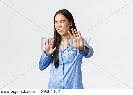 Digusted And Displeased Asian Girl In Blue Pajamas Extend Hands Forward In Refusal, Rejecting Someth