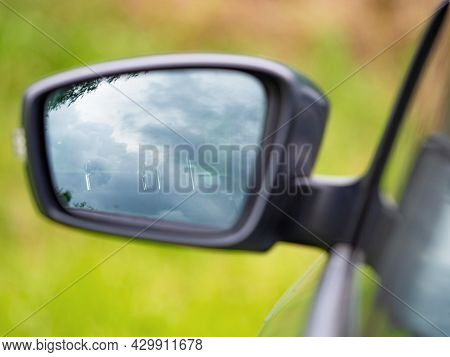 Left Rear View Mirror Of The Car With Unclear View To Driver Seat. The Outback Road With Blurred Gre