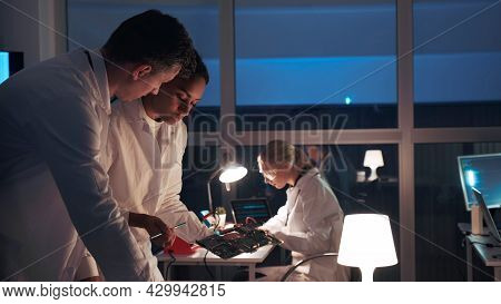 Side View Of Two Electronics Development Engineers Talking About Motherboard And Explaining Details 