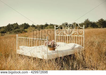 Photo Shoot In Nature, Wrought Iron Bed With White Linen Standing In Center With Basket Of Wildflowe