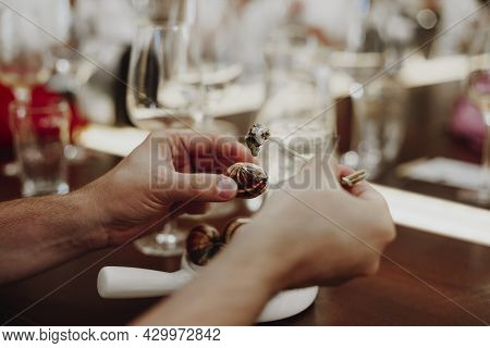 Cropped Picture Of Man Eating Escargots With Special Fork, White Ceramic Pan With Cooked Snails, Sit