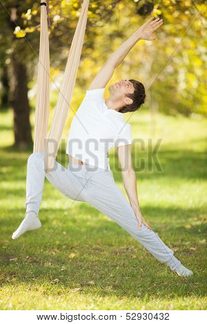Anti-gravity Yoga, man doing yoga exercises in the park