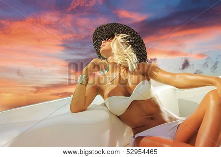 Young sexy woman on her private yacht at sunset