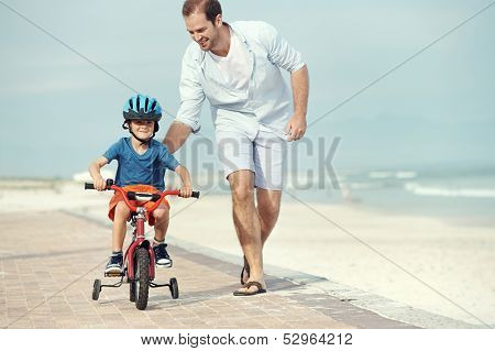 Father and son learning to ride a bicycle at the beach having fun together