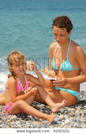 Krásná žena s hezká holčička se naklonil Seashell mísa s uchem na kamenné Seacoast
