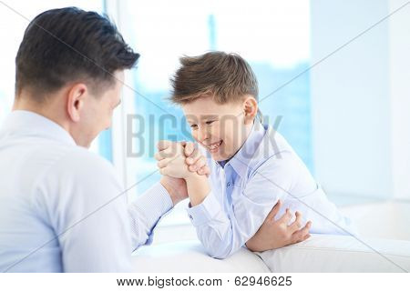 Photo of little boy and his dad armwrestling