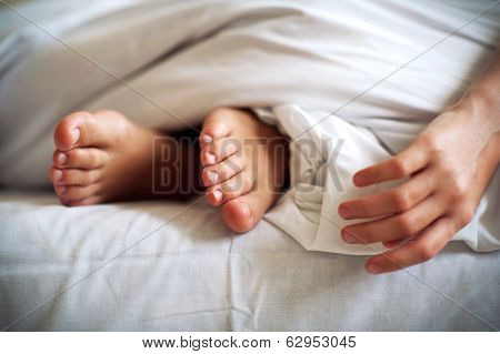 Sleeping Child Barefoot Feet And Hand On White Bed Linen. Indoors.