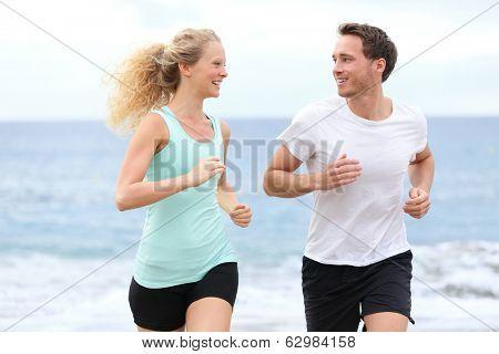 Running couple jogging exercising on beach talking and training as part of healthy lifestyle. Two fit runners jogging happy and smiling during workout.
