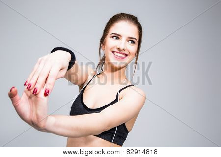 Portrait of a smiling sports woman stretching hands over gray background