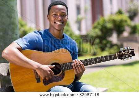 cheerful young african american man playing guitar outdoors