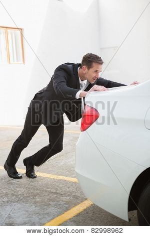 Businessman pushing his broken down car in a car park