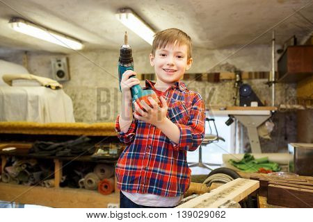 children, carpentry, profession and people concept - happy little boy with drill at workshop
