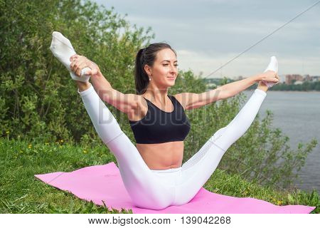 Woman holding legs apart doing exercises aerobics warming up with gymnastics for flexibility leg stretching workout outdoors