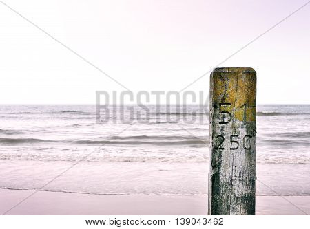 Wooden pillar or pile at the beach. Beach section stake with engraved or carved numbers. Sunset at the beach with selective focus on the foreground and copy space.