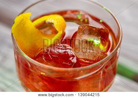Dark orange cocktail in glass. Piece of lemon peel. Taste of dry gin. Cold and fresh negroni.