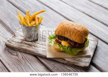 Burger and bucket of fries. Hamburger on piece of paper. Delicious fast food meal. Traditional recipe of beefburger.