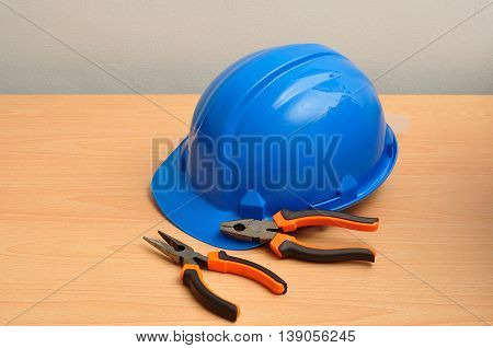 A blue hard hat displayed with a set of pliers and a long nose pliers