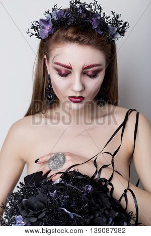 Beautiful cheeky girl in the image of a vampire with bright dark makeup, black vampire bride with a bouquet and a black wreath