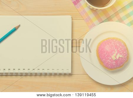 Strawberry Donut with notebook in vintage tone. Donut on plate with cup of coffee with writing equipment.