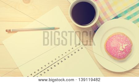 Strawberry Donut with notebook in vintage tone. Donut on plate with cup of coffee with writing equipment.