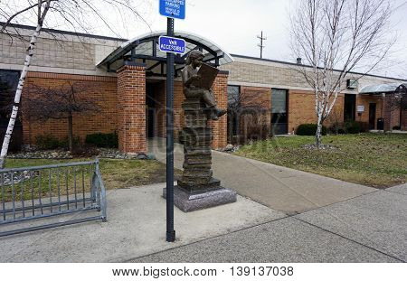 CADILLAC, MICHIGAN / UNITED STATES - DECEMBER 26, 2015: A sculpture of a girl reading a book, while sitting atop a tall pile of books, stands in front of the Cadillac Public Library.