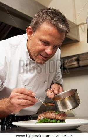 Chef Adding Sauce To Dish In Restaurant Kitchen