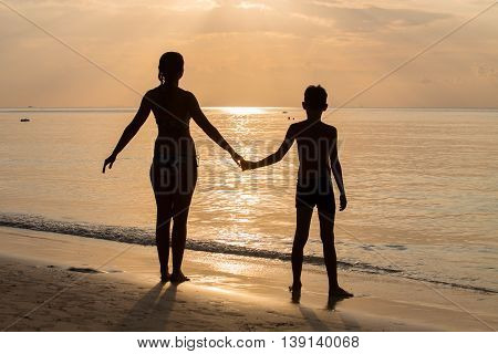 Silhouette mother with her son on the beach during sunset. Thailand