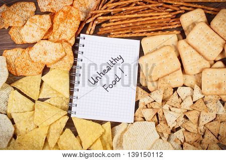 Inscription Unhealthy Food In Notebook And Heap Of Crisps And Cookies