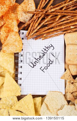 Inscription Unhealthy Food In Notebook And Heap Of Crisps And Cookies