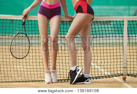 Two sexy slim fitness woman long legs in sports clothing holding tennis racket on clay court
