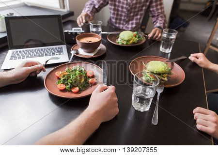 Closeup picture of vegan dishes represented onblack wooden table in vegan restaurant or cafe while business people communicating. Laptop computer.