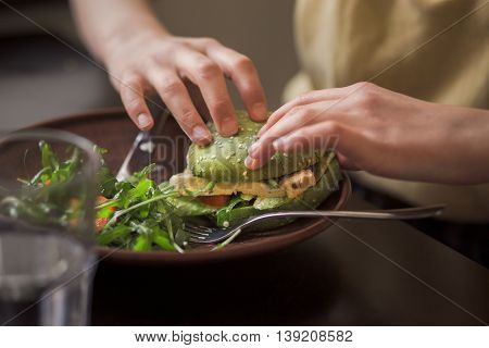 Picture of vegan dish represented on wooden plate. Lady's hands taking vegan burget from plate in vegan restaurant or cafe.