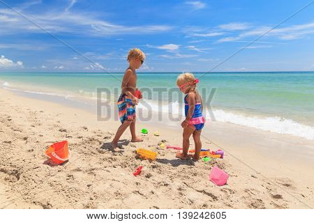 little boy and girl play with sand on summer beach