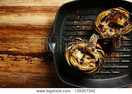Baked artichokes in black grill pan on wooden background