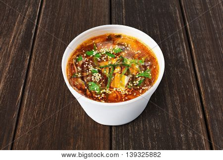 Japanese cuisine hot food delivery - miso soup at brown wooden background in white plastic plate